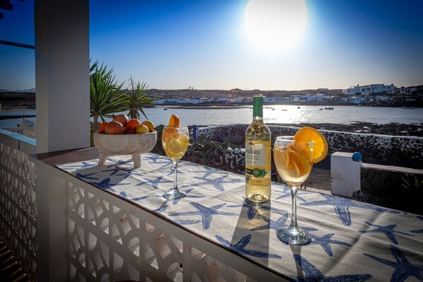 A table with a bottle of Albi wine, two glasses, and a bowl of fruit on a balcony overlooking a coastal town. - Beautiful house seafront (CN)