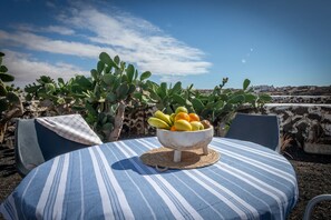 A table with a striped tablecloth and a wooden bowl filled with fruits, surrounded by cacti and a clear sky. - Beautiful house seafront (CN)