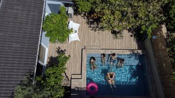 An aerial view of a swimming pool with four people, surrounded by trees and a covered seating area.