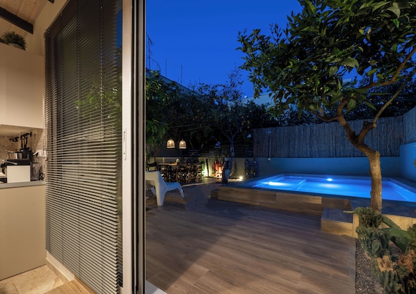 A modern outdoor patio with a hot tub, wooden flooring, and a dining area with tables and chairs.