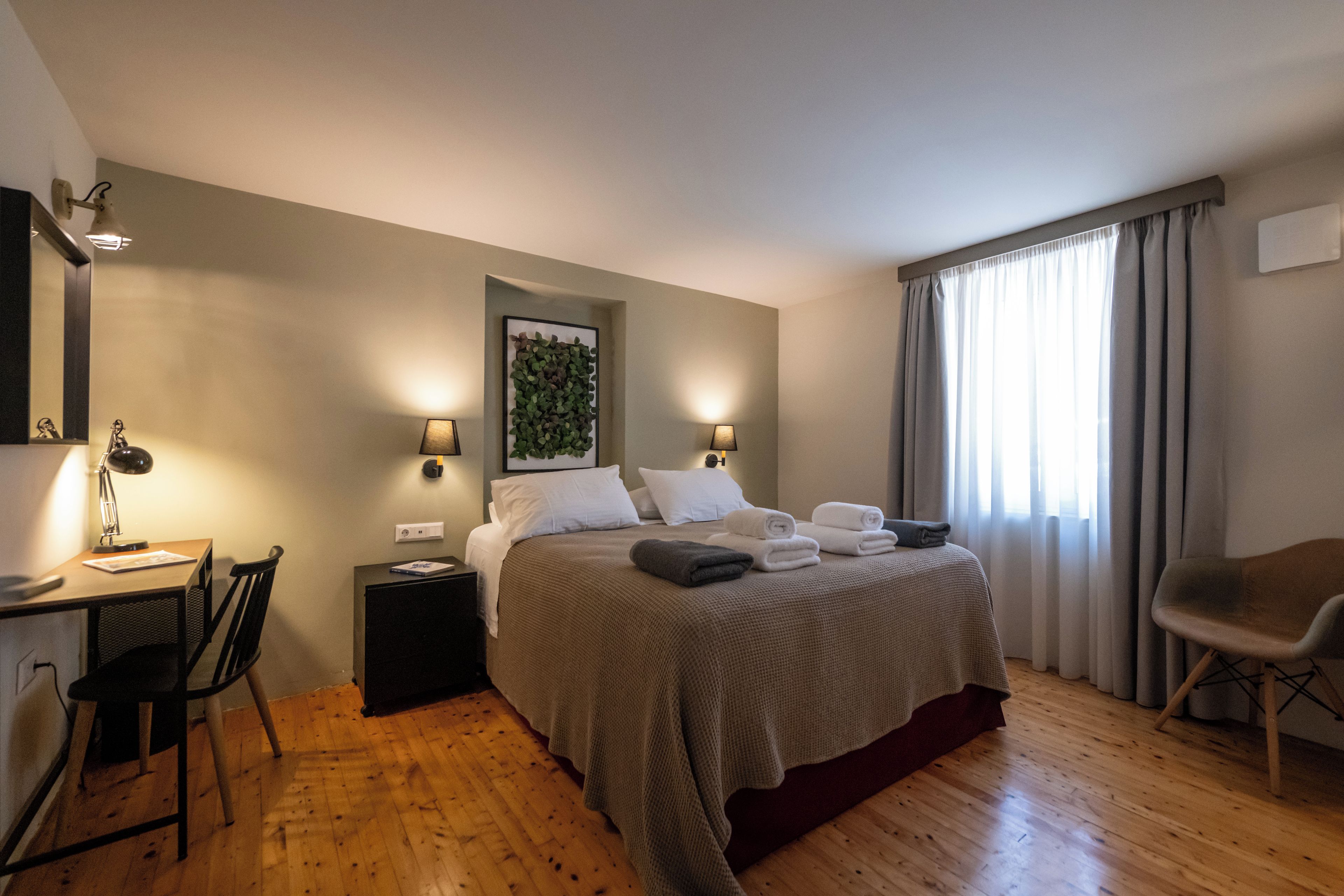 Une chambre d’hôtel comprenant un lit, un bureau avec une chaise, une table de chevet et une fenêtre avec des rideaux.