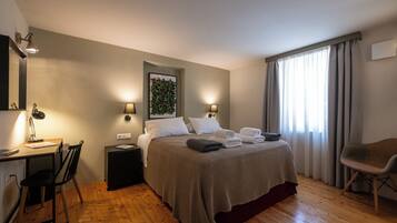 Une chambre d’hôtel comprenant un lit, un bureau avec une chaise, une table de chevet et une fenêtre avec des rideaux.