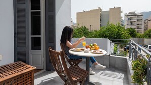 Una mujer sentada en una mesa redonda en un balcón, con vistas a edificios y zonas verdes.