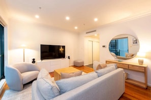 Uma sala de estar moderna com sofá, poltrona, TV e um espelho redondo na parede.