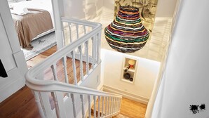 A staircase with white balusters and a white railing, leading to a room with a patterned rug and a bed.