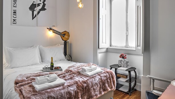 A neatly arranged bedroom with a bed, a guitar, a window, and a small table with a vase.
