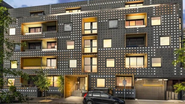 Ein modernes, mehrstöckiges Gebäude mit dunkler Fassade, mehreren Balkonen und einem davor stehenden Auto.