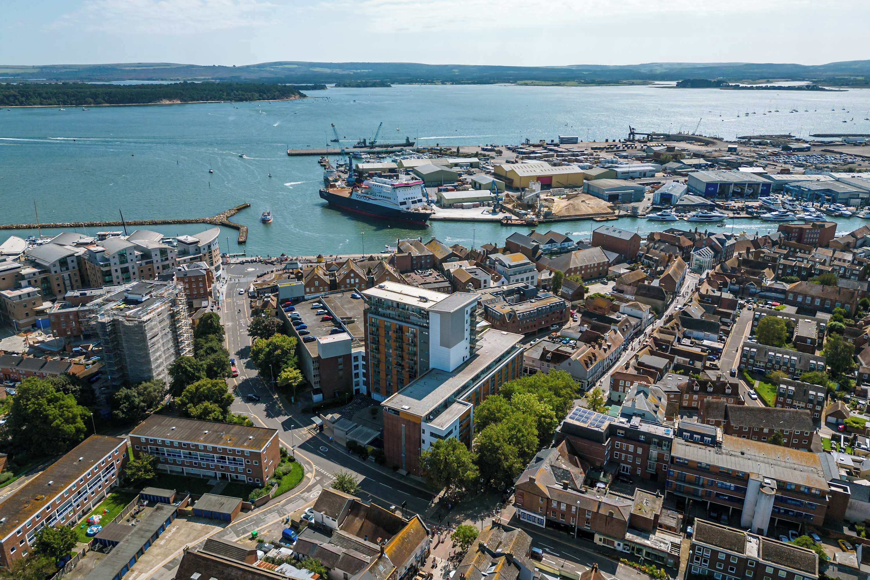 Ett flygbildsbild av en kuststad med en småbåtshamn, byggnader och ett stort fartyg som ligger förtöjt i hamnen.