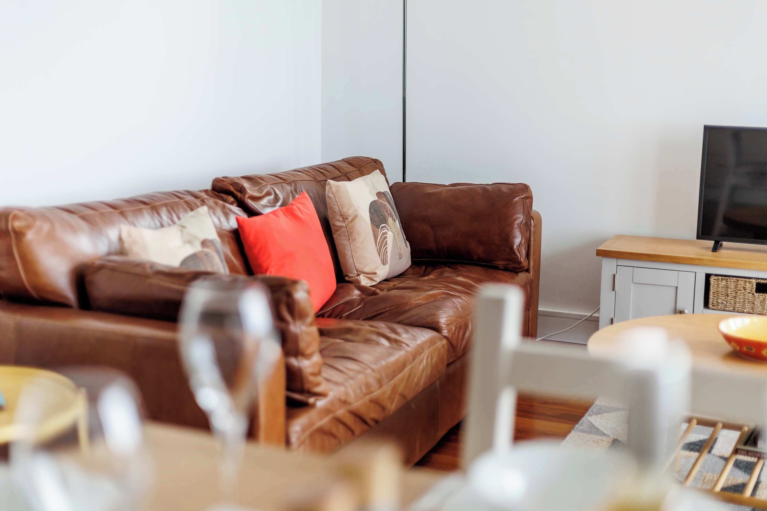 Ein braunes Ledersofa mit Kissen, einem Fernseher und einem kleinen Holztisch mit einer Schüssel.