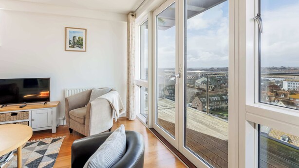 A modern living room with a large window, a flat-screen TV, a sofa, and a dining table.