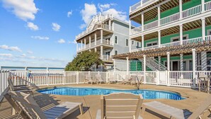 A pool area with lounge chairs and a view of a building with multiple balconies. - Premier Soundfront Dog Friendly Oasis w/ Pool, Hot Tub, Elevator, and Much More! (Avon)