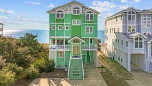 A multi-story building with a green and white color scheme, a front entrance, and a staircase leading to the entrance. - Premier Soundfront Dog Friendly Oasis w/ Pool, Hot Tub, Elevator, and Much More! (Avon)