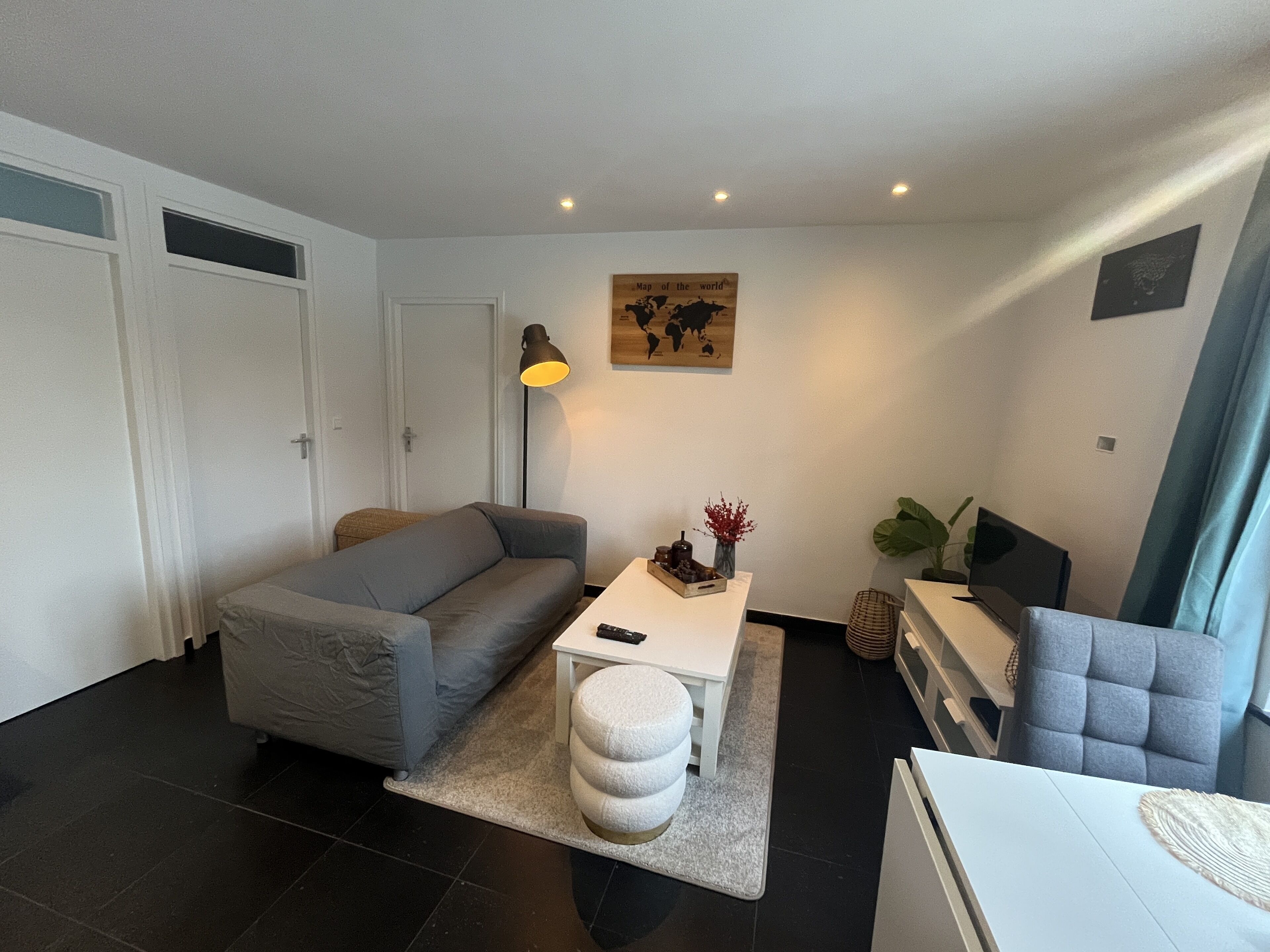 A modern living room with a grey sofa, a white coffee table, and a small ottoman. There is a world map on the wall and a plant on the side.