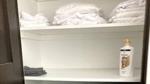 A closet with neatly folded towels in white, gray, and black, and a bottle of Pantene shampoo. - G’s Home Away From Home (Iowa City)