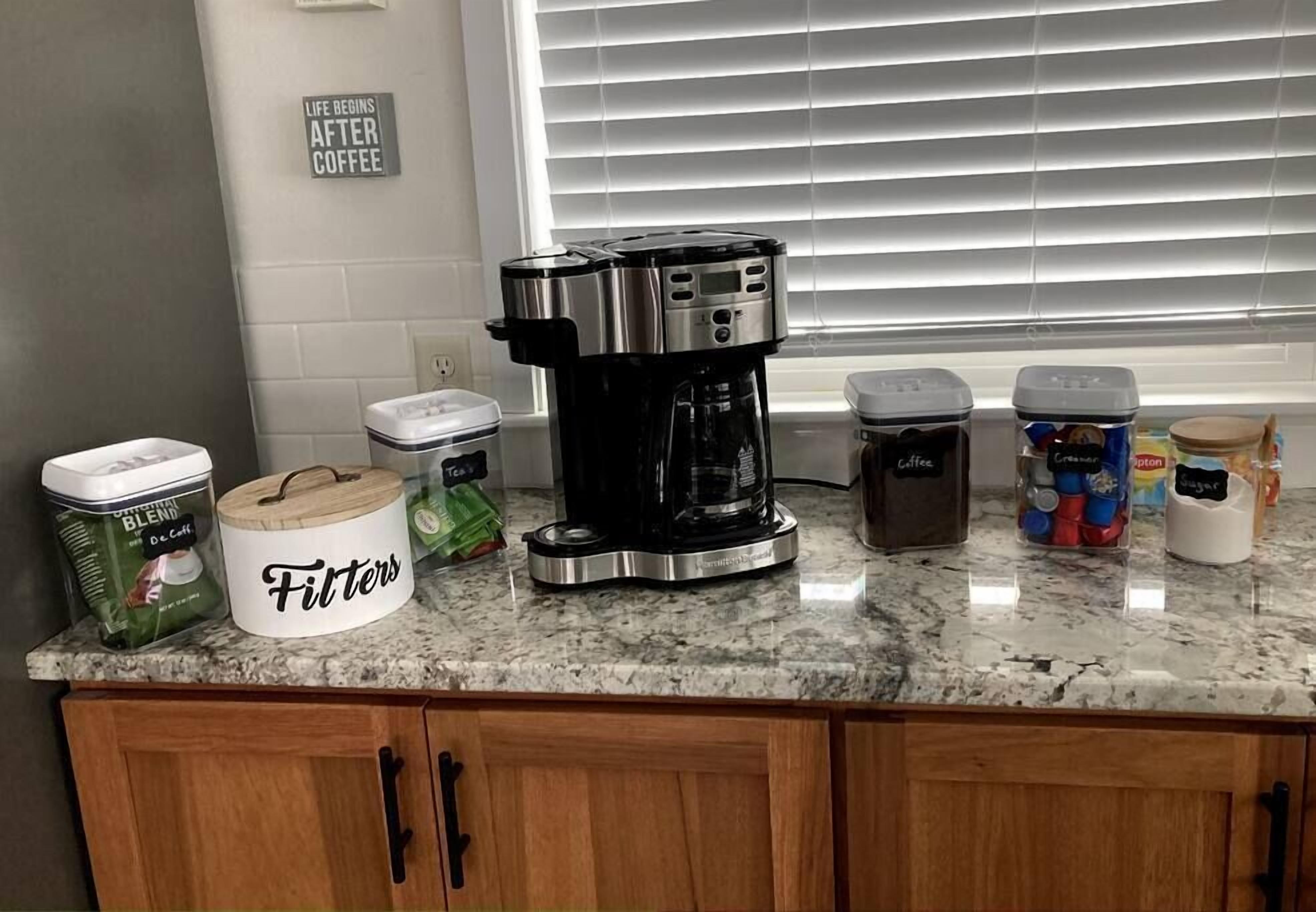 Un piano di lavoro in cucina con una macchina da caffè, un contenitore con l'etichetta 'Filtri' e diverse cialde per caffè.