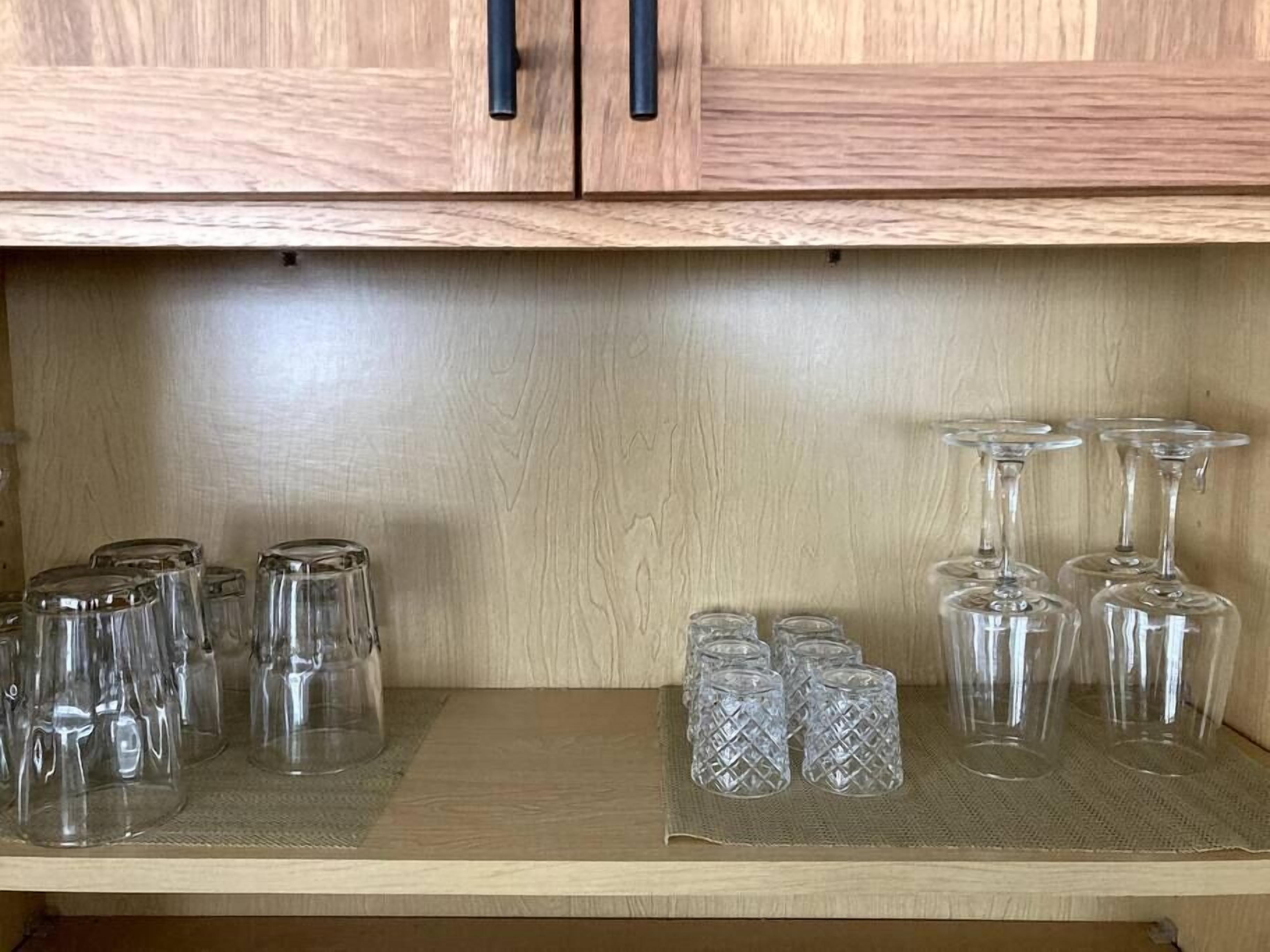 Een houten kastje met twee zwarte handgrepen, met daarin verschillende glazen, zoals bolglazen en wijnglazen.