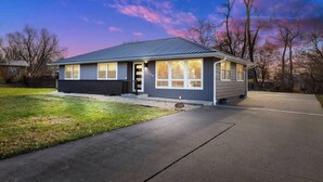 A single-story house with a dark gray exterior, a front door, and a garage. - G’s Home Away From Home (Iowa City)