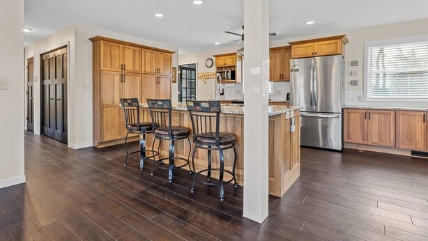 A modern kitchen with wooden cabinets, stainless steel appliances, and a central island with bar stools. - G’s Home Away From Home (Iowa City)