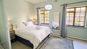 A bedroom with a bed, nightstands, a mirror, and a window with curtains. - Beachside 2BD Home in the Heart of Sea Point! (Cape Town)