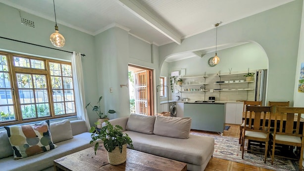 A living room with a sofa, coffee table, and a view of the kitchen. - Beachside 2BD Home in the Heart of Sea Point! (Cape Town)