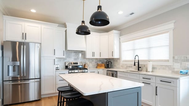 A modern kitchen with white cabinets, a stainless steel refrigerator, a large island with stools, and pendant lighting. - Modern 4BR Oasis - Main Level Master + 2 King Beds (Forest)