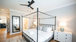 A four-poster bed with a ceiling fan, a bedside table with a lamp, and a nightstand with drawers. - Modern 4BR Oasis - Main Level Master + 2 King Beds (Forest)