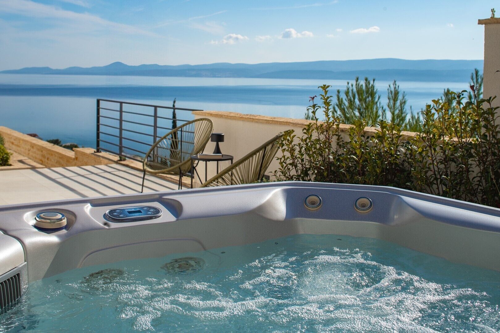 Un bain à remous équipé d’un panneau de commande, d’un siège et offrant une vue sur la mer et les montagnes.