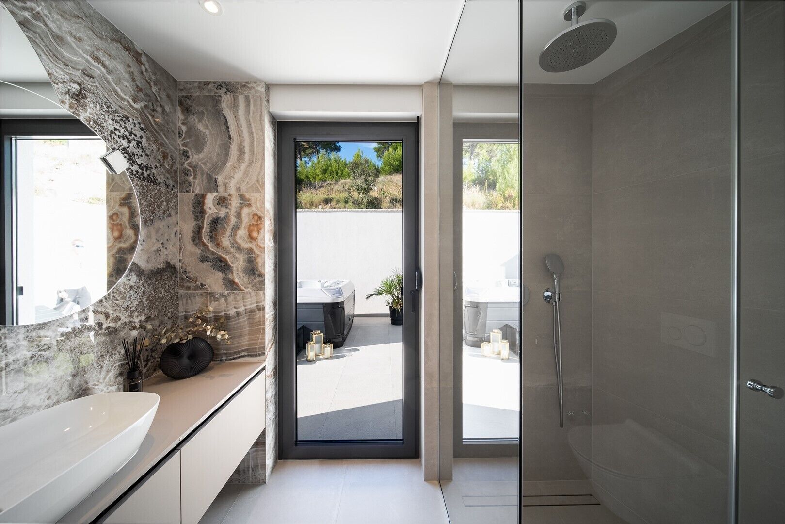 A modern bathroom with a large marble sink, a glass shower enclosure, and a view of the outdoors.