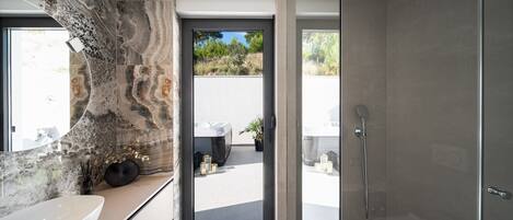 A modern bathroom with a large marble sink, a glass shower enclosure, and a view of the outdoors.