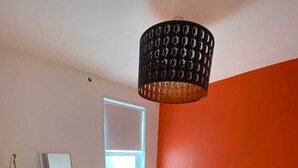 Un dormitorio con cama, mesita de noche, ventana y lámpara colgante.