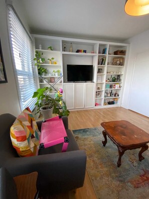 A living room with a sofa, a coffee table, a TV, and a bookshelf filled with various items. - Vibrant & Funky 1BD Flat - 12 Mins to Stratford! (London)