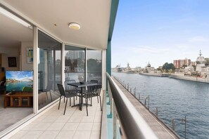 A balcony with a table and chairs, overlooking a body of water with buildings and a bridge in the background. - Apartment in Iconic Fingerwharf (Woolloomooloo)