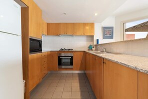 A compact kitchen with wooden cabinets, a gas stove, a microwave, and a sink. - Apartment in Iconic Fingerwharf (Woolloomooloo)
