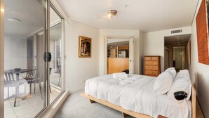A bedroom with a bed, a wooden nightstand, a dresser, and a glass door leading to a balcony. - Apartment in Iconic Fingerwharf (Woolloomooloo)
