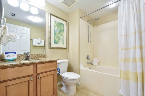 Une salle de bain équipée d’un lavabo, de toilettes et d’une baignoire. On y trouve un porte-serviettes avec des serviettes et un tableau encadré accroché au mur.