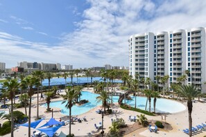 Un complexe hôtelier doté d’une grande piscine, de palmiers et d’un immeuble de grande hauteur en arrière-plan.