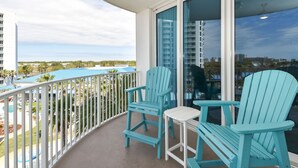 Een balkon met twee turkozen Adirondack stoelen en een kleine witte tafel, met uitzicht op een zwembad en een stadsbeeld.