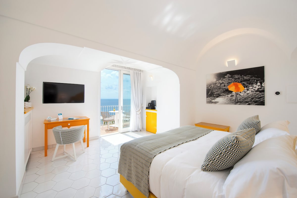 A hotel room with a bed, a desk, a chair, a TV, and a balcony with a view.