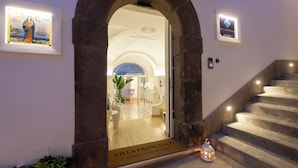 A grand entrance with a stone archway leading to a well-lit interior. A sign on the door reads "Villa Francesco Luxury Suites Posturno." - Villa Francesco Luxury Suites (Positano)
