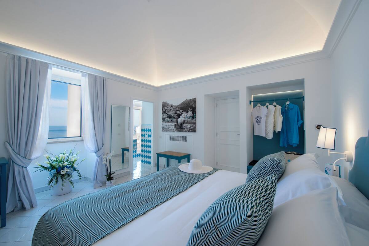 A modern hotel room with a large bed, a walk-in closet, and a view of the sea.