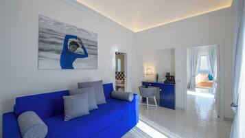 A modern living room with a blue sofa, a coffee machine, and a view into the dining area.