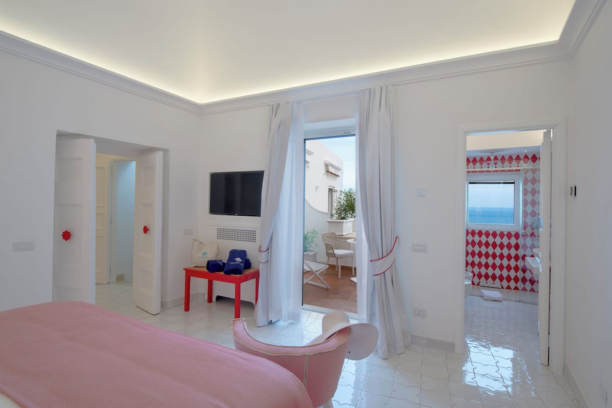 A hotel room with a bed, a TV, a small table with a chair, and a view of the outside.