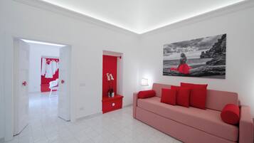 A modern room with a red sofa, a red bedside table, and a red door. There is a white chair and a white wardrobe in the background.