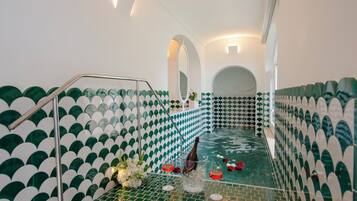 Un área de spa con suelo de baldosas, una piscina pequeña y una zona de estar con una botella de champán y copas.