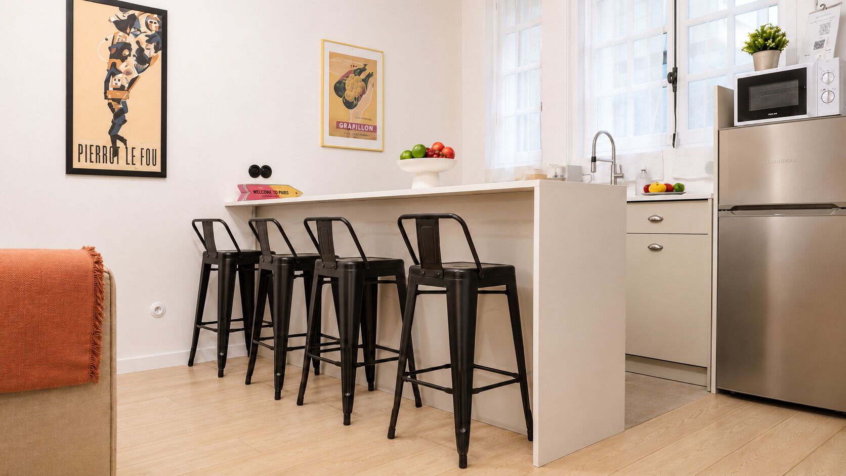 Una cocina moderna con una isla central, taburetes negros, un refrigerador de acero inoxidable y un microondas en la encimera.