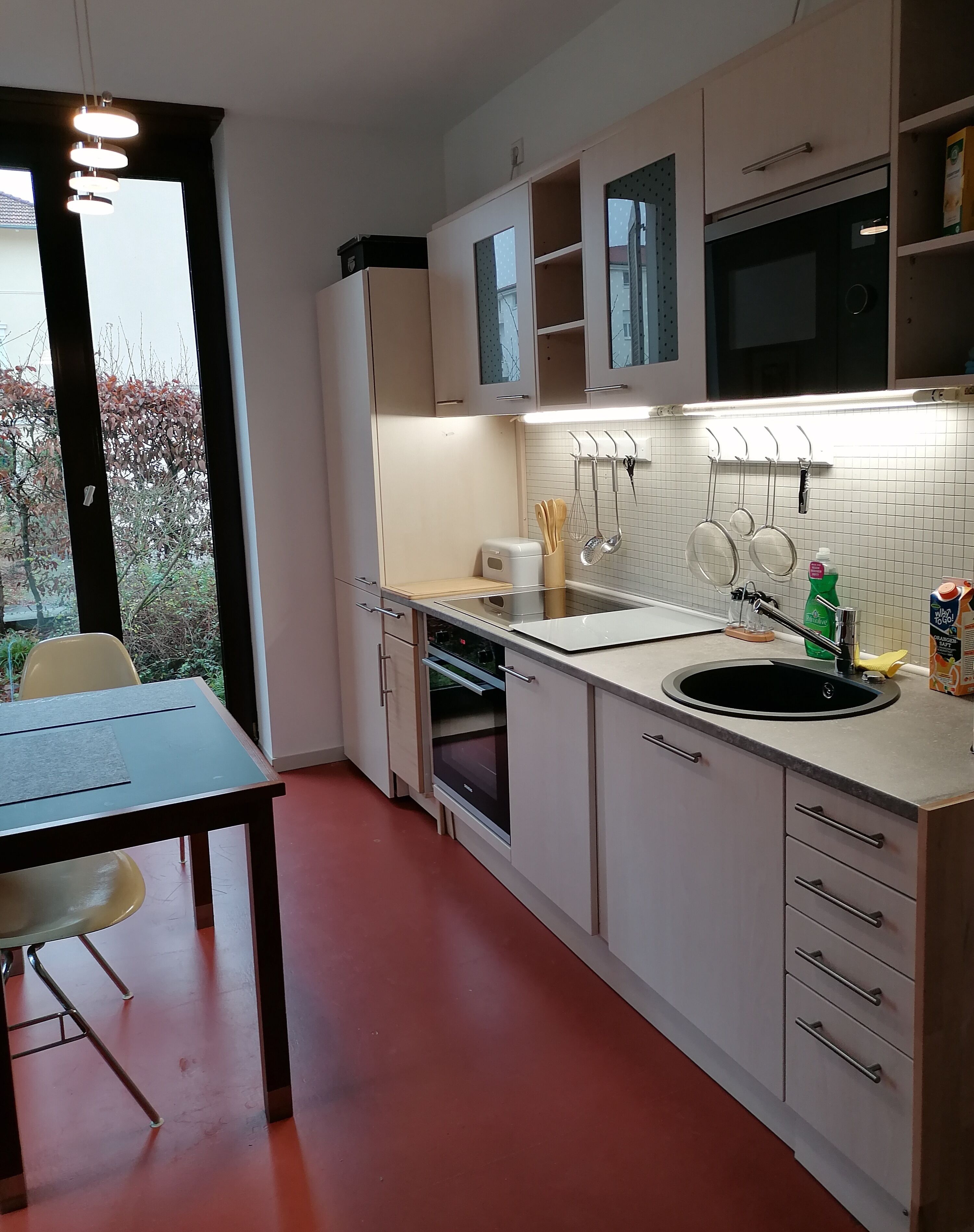 Una cocina moderna con armarios blancos, horno empotrado, lavamanos y comedor con mesa y sillas.