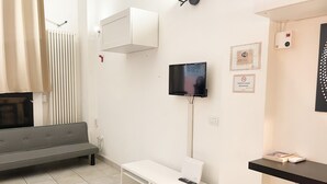 Un salon moderne avec un canapé gris, un meuble de rangement blanc pour les appareils électroniques, un téléviseur à écran plat fixé au mur et une petite table avec une télécommande.