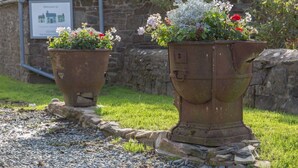 Two large, rusted planters with flowers and a stone wall in the background. - The Tack Room, shared hot tub and sauna (Hartland)