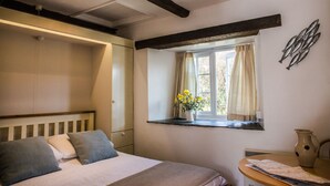 A bedroom with a bed, a bedside table, a window with curtains, and a wall-mounted decoration. - The Tack Room, shared hot tub and sauna (Hartland)