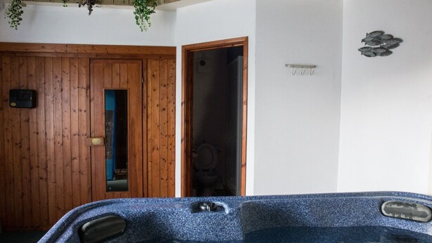 A room with a wooden door, a bathroom with a toilet, and a hot tub with water jets. - The Tack Room, shared hot tub and sauna (Hartland)